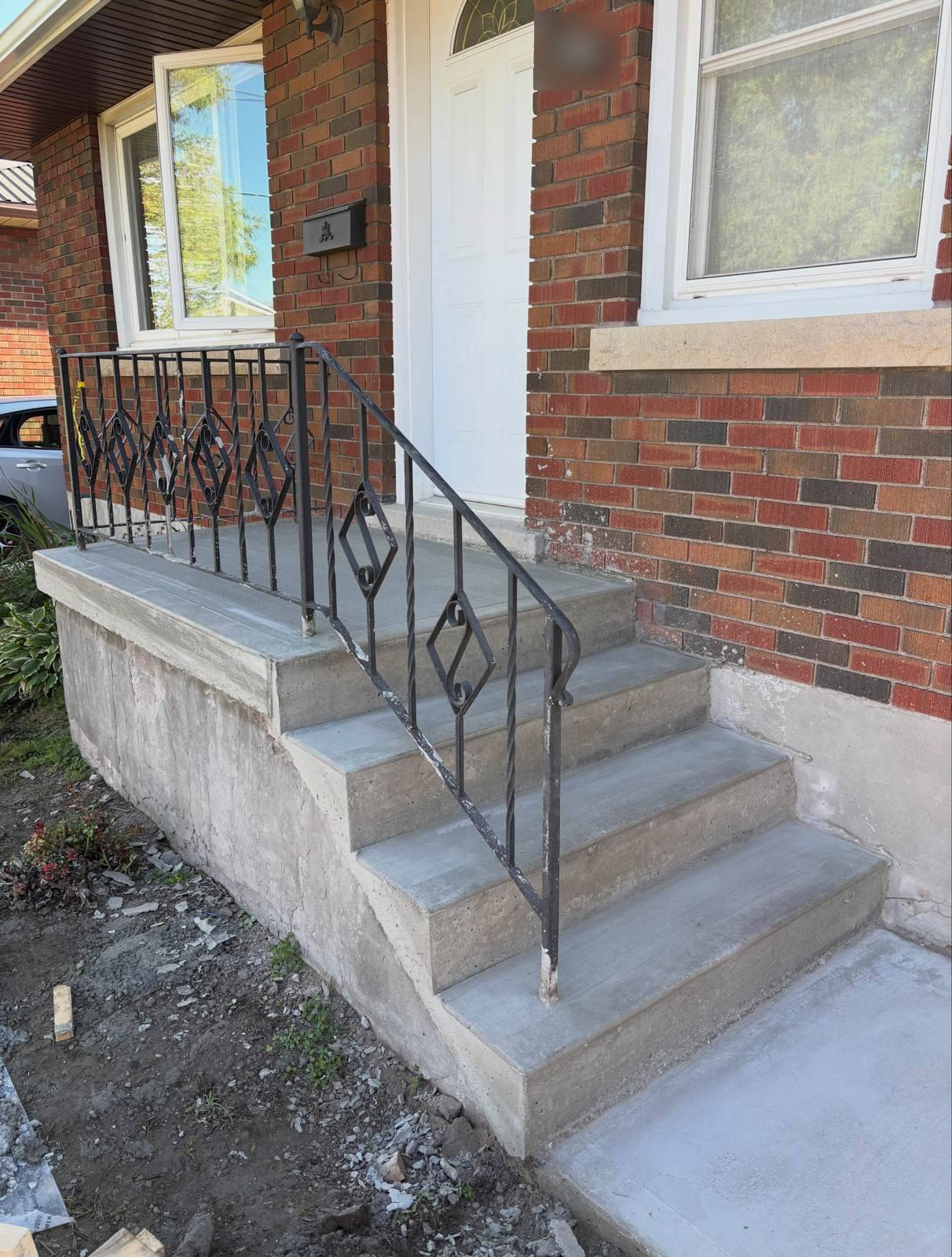 Smooth concrete front steps with a black railing on a brick house